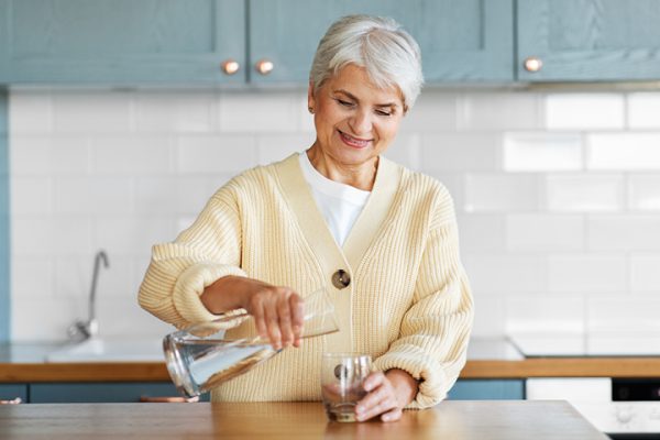 Elderly woman pouring a glass of water from a pitcher